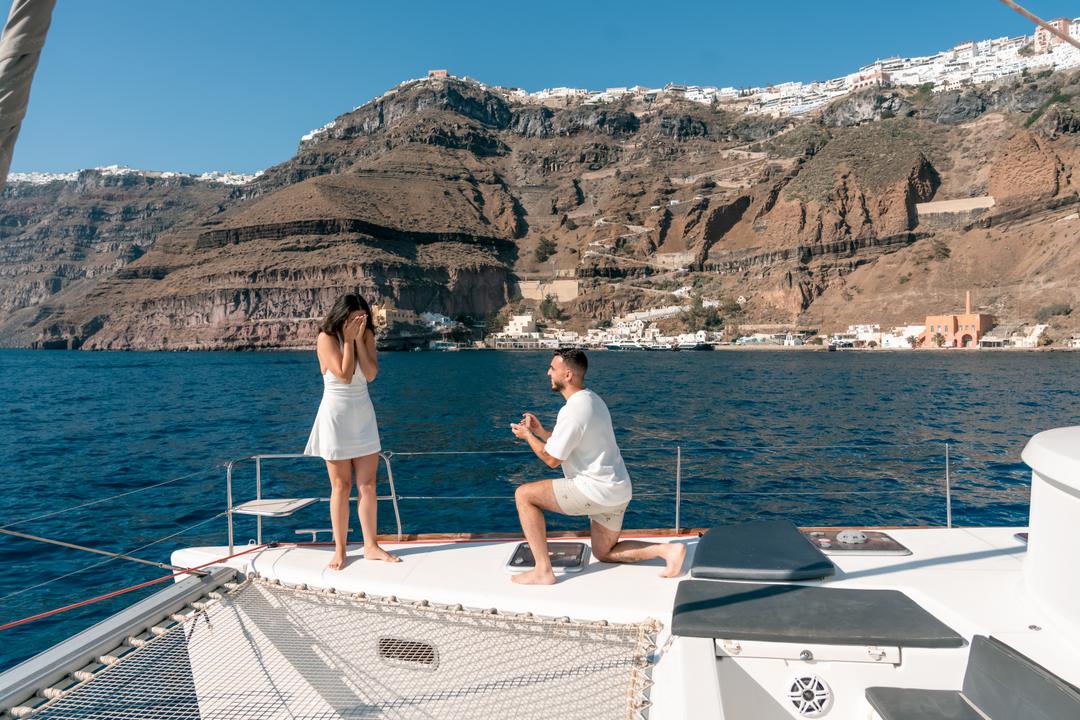 Kneeling on the bow of a catamaran below the caldera cliffs of Santorini