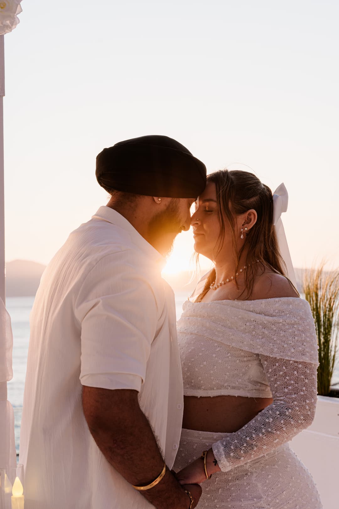 Foreheads together at sunset, the sun burning low between their faces and the sea pale behind