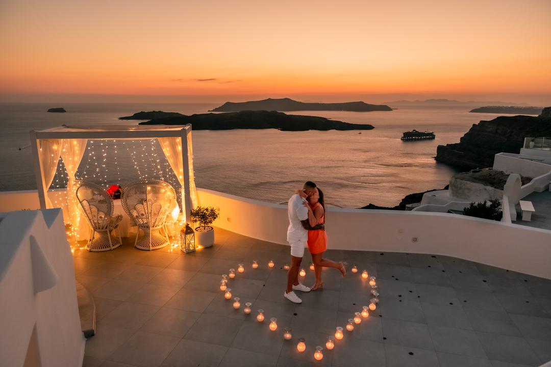 An elevated dusk frame of a candle heart and glowing canopy on a caldera terrace