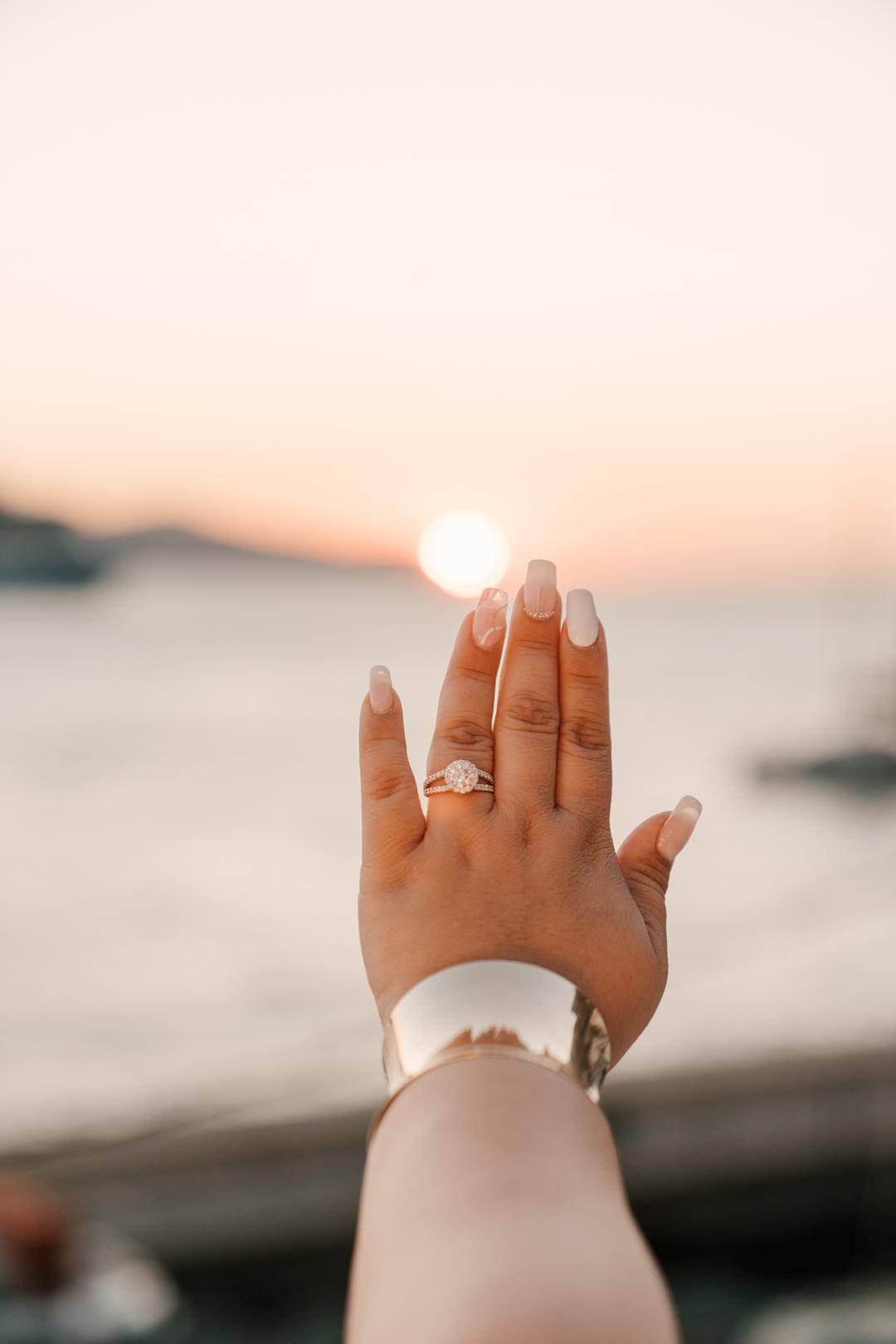 A hand raised against the setting sun, a new ring on the finger and the sea below