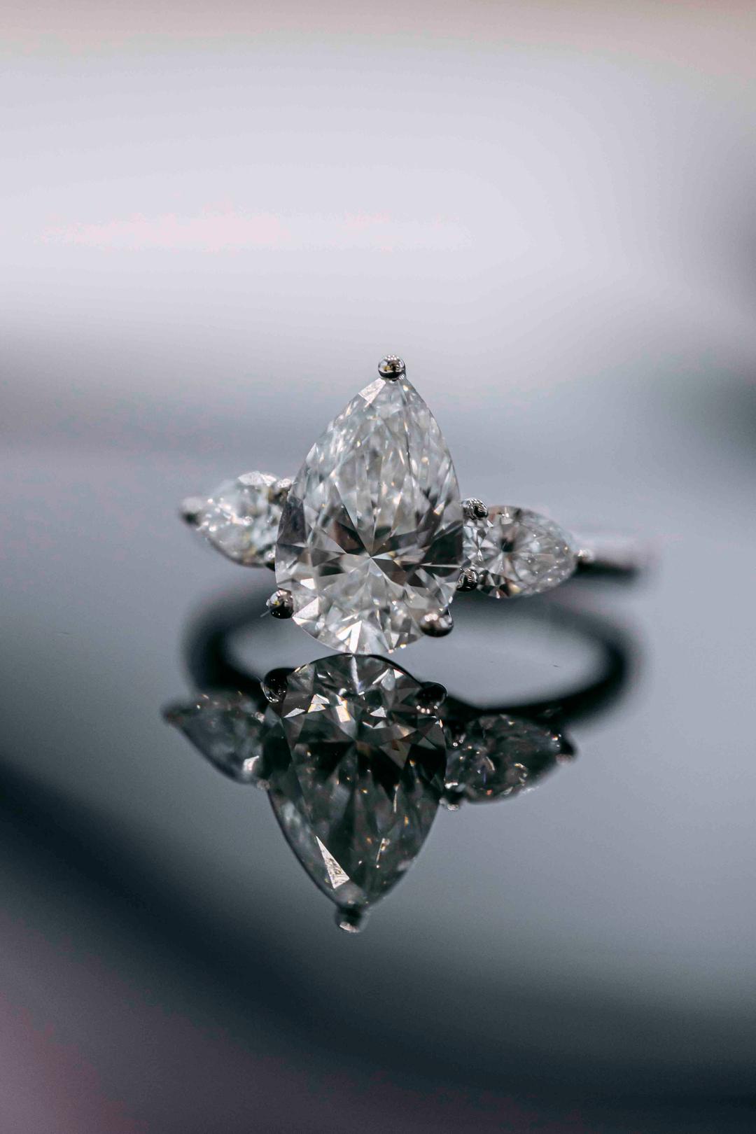 A marquise-cut engagement ring photographed close, reflected in the pale surface it stands on
