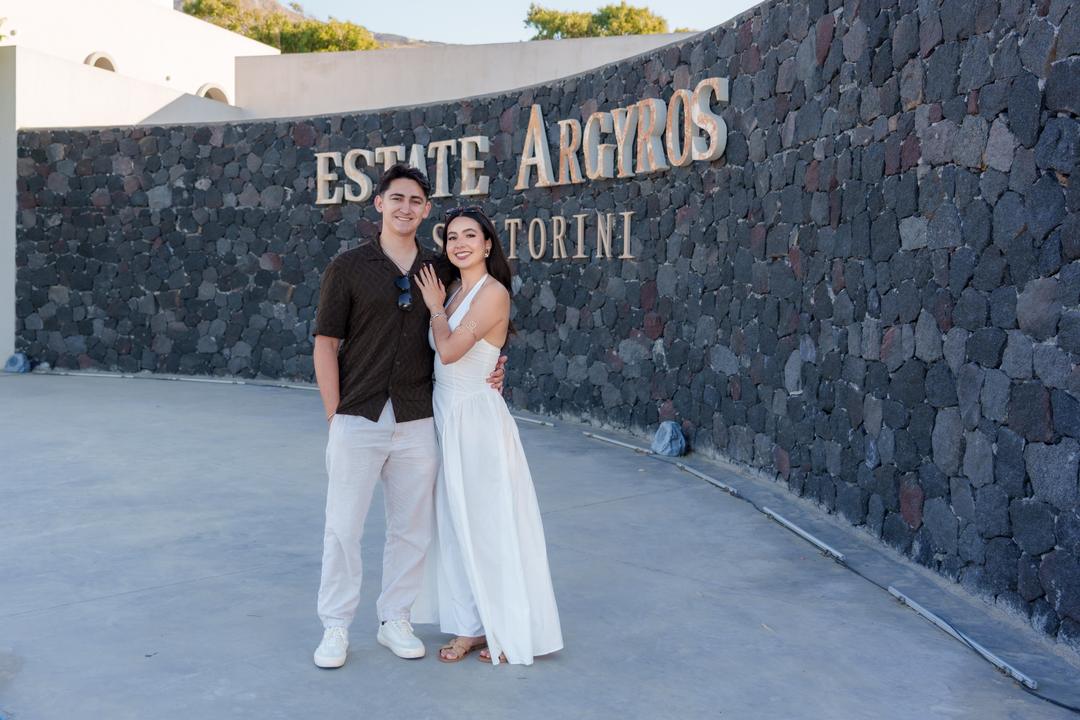 A couple standing against the curved black stone wall and lettering of Estate Argyros