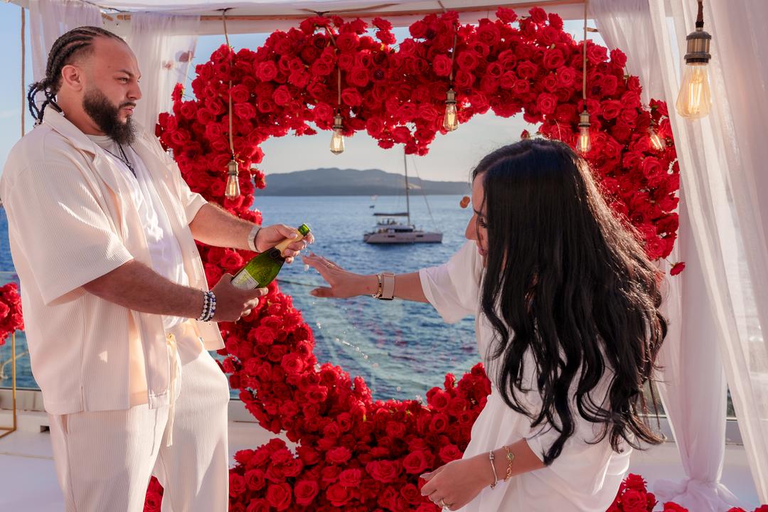 Popping a champagne cork inside a heart of red roses