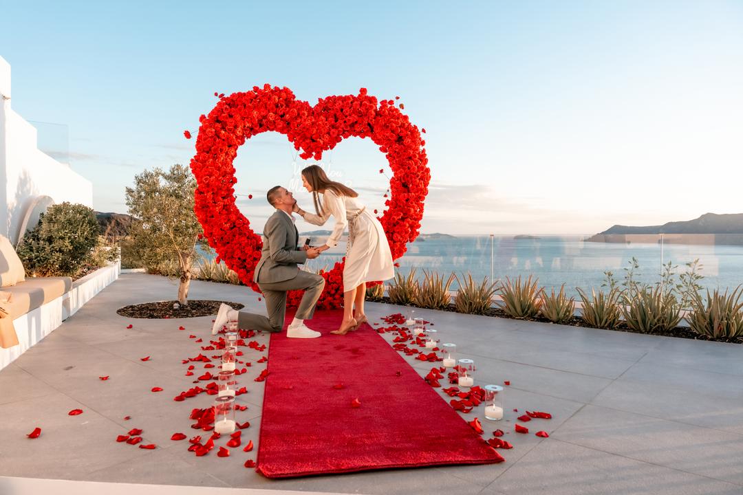 A kiss inside a red-rose heart arch on a caldera terrace