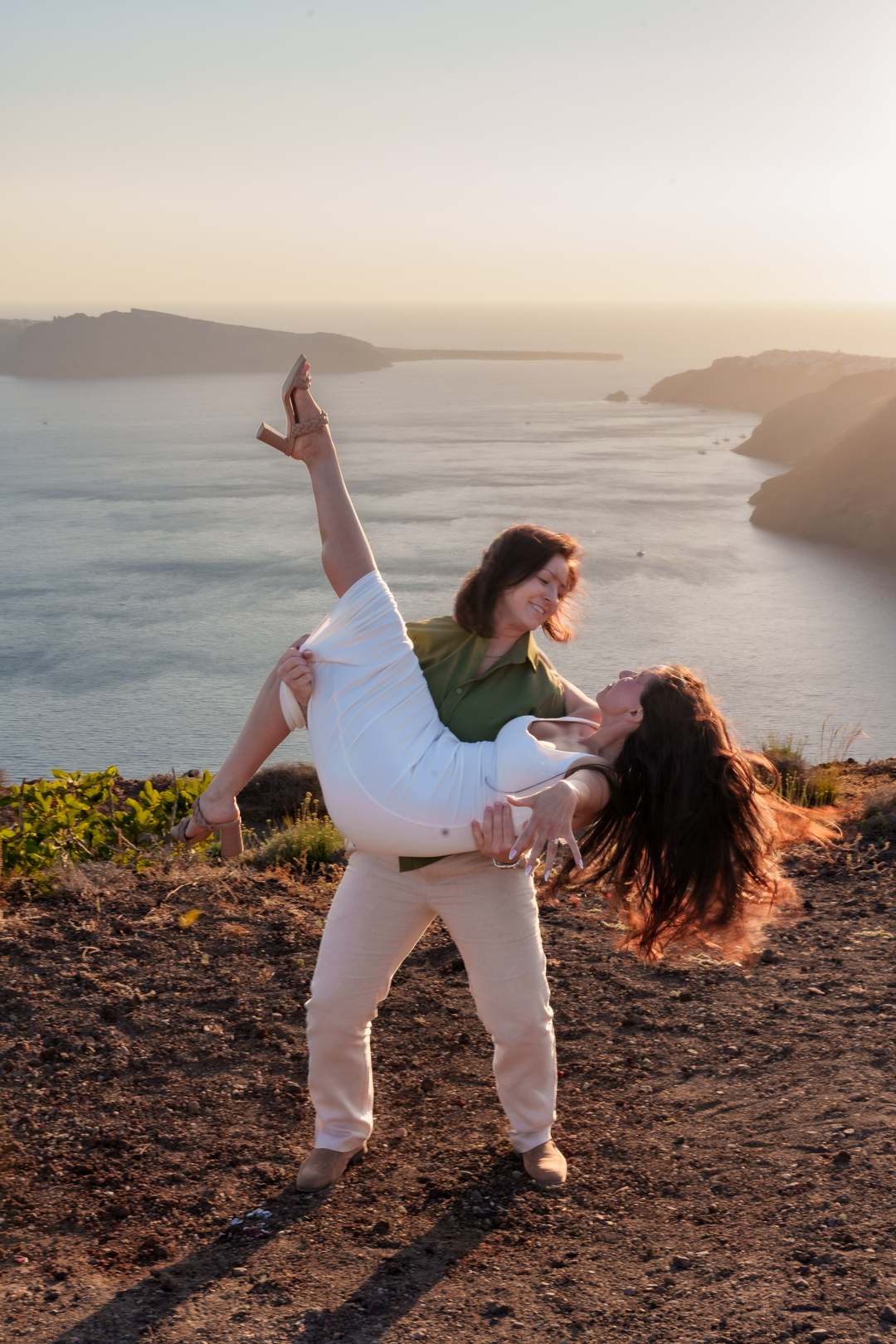 One partner lifting the other mid-laugh at golden hour above the sea