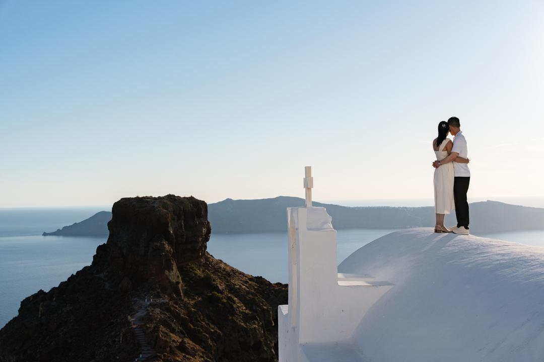 A couple above the caldera with Skaros Rock rising behind them at Imerovigli