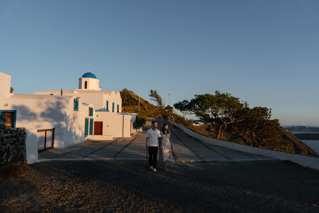 A couple walking a quiet whitewashed rim lane in late light, nobody else in sight