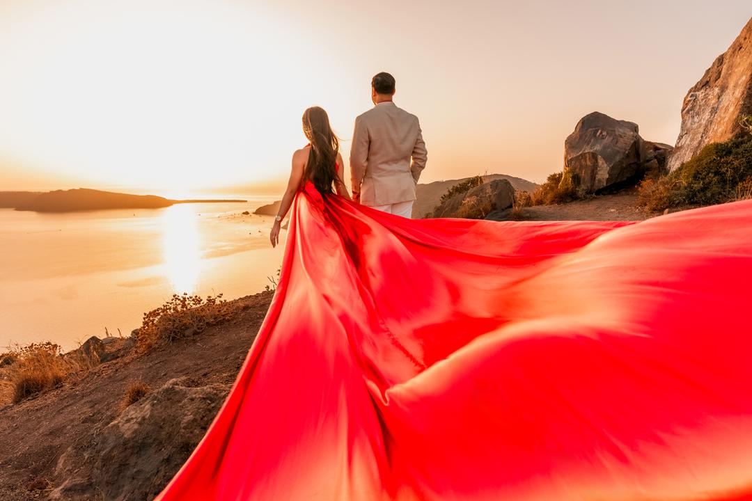 A red flying dress mid-toss on the caldera rim at golden hour