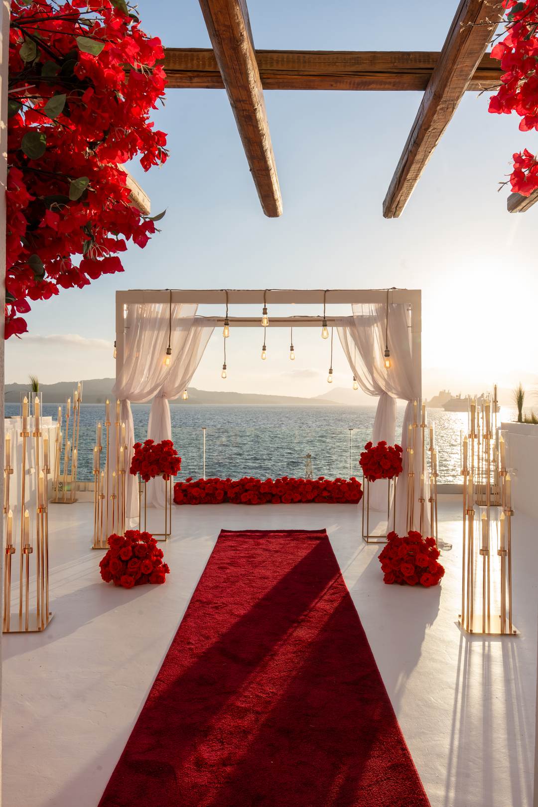 A production-scale scene: red roses, candelabras and a red carpet on a terrace at golden hour