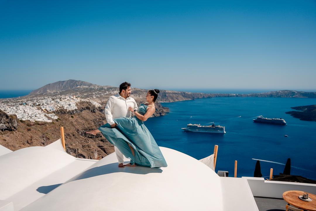 A couple on a whitewashed rooftop high above the caldera, ships small on the water below