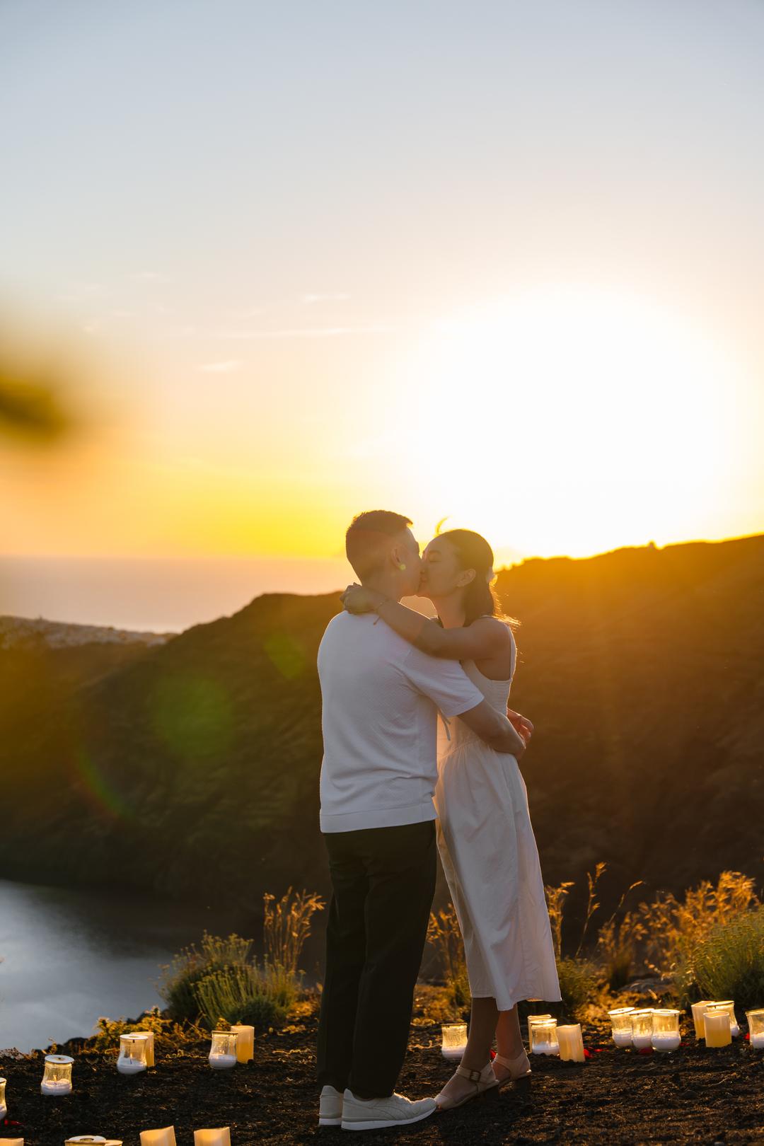 A couple embracing on the caldera rim as the sun drops behind the far islands
