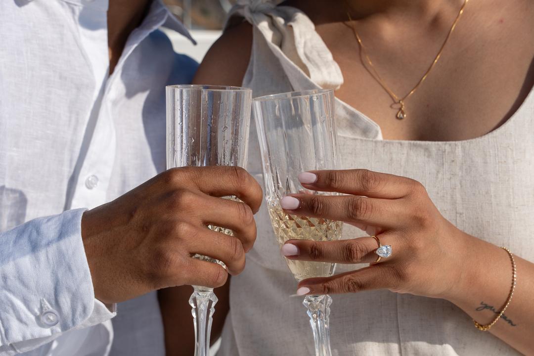 Two champagne glasses touching, a new ring on the hand holding one of them
