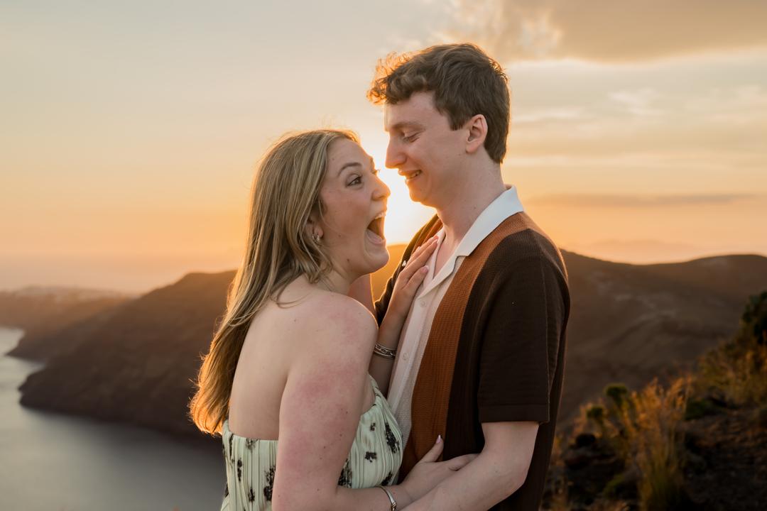 A couple holding each other on the rim at sunset, she is laughing over her shoulder and the sky behind has gone amber