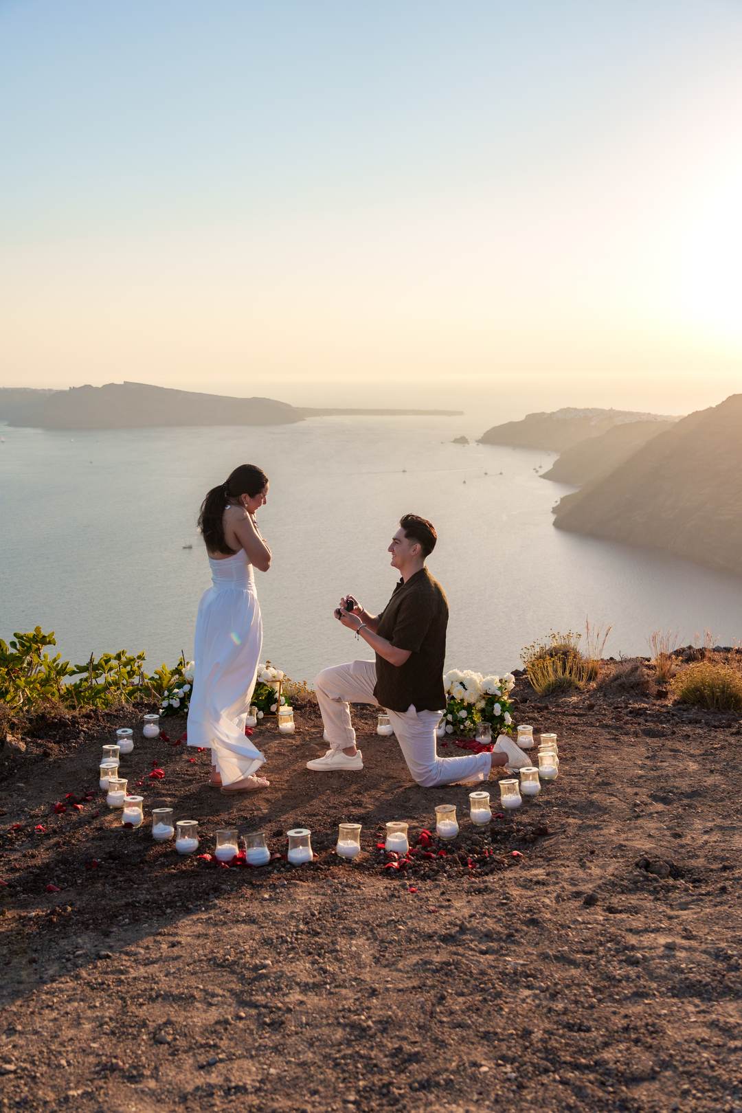 A man on one knee inside a ring of candles on the caldera rim as the sun drops behind the far side