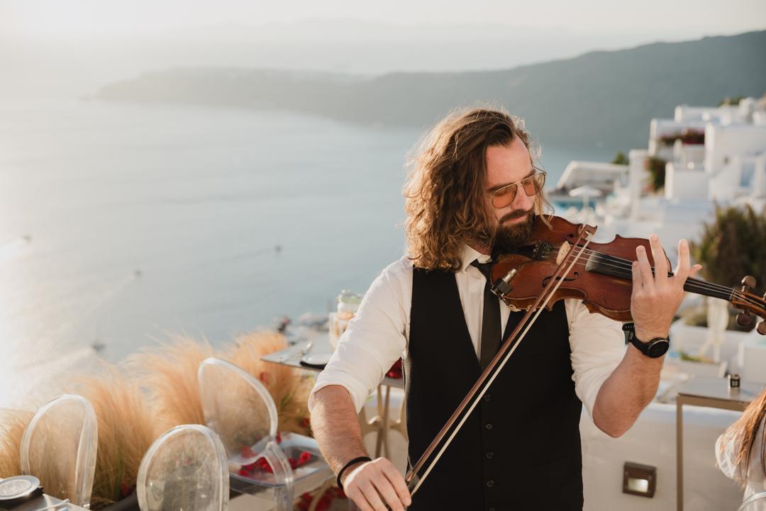 A violinist playing on a terrace above the caldera in low golden light