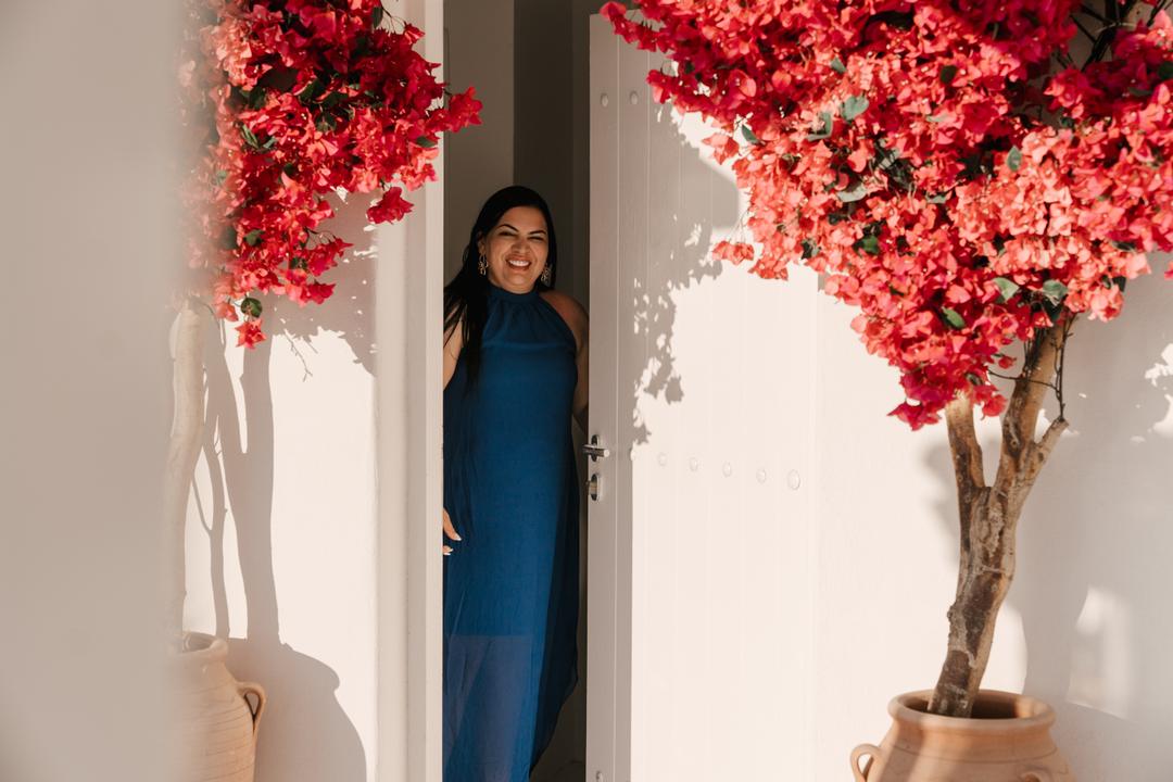 A woman standing in a white doorway between two bougainvillea in full red flower in terracotta pots