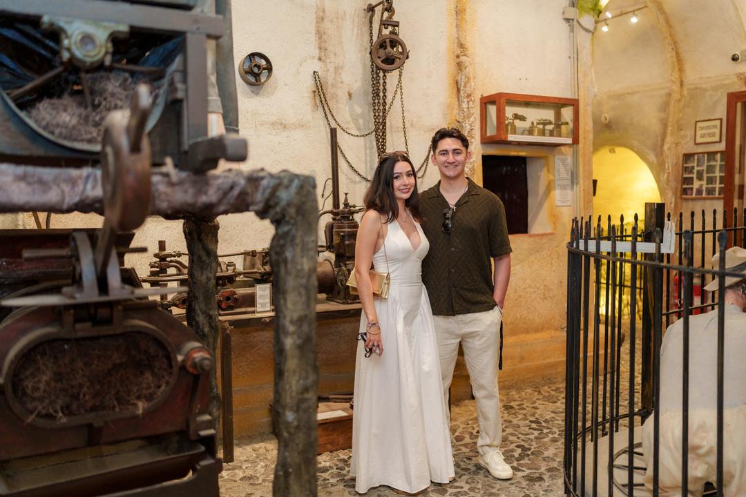 A couple in the vaulted stone hall of a wine museum beside an old wooden grape press
