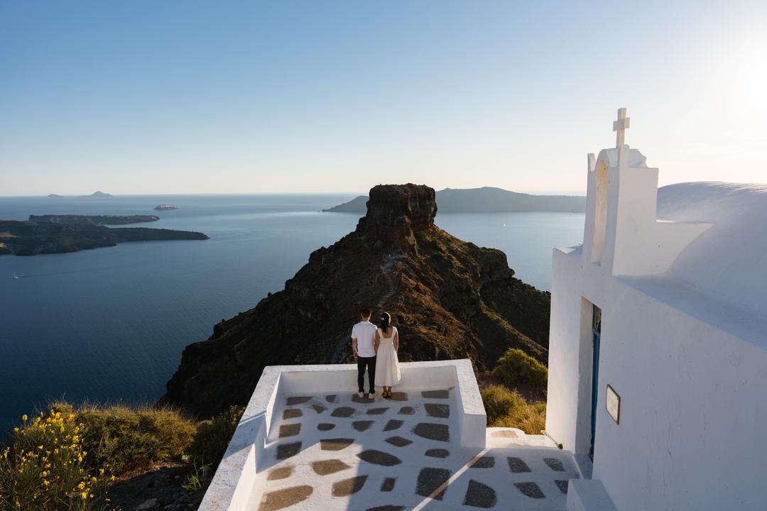 Skaros Rock from a whitewashed chapel terrace at Imerovigli, a couple standing at the edge above the caldera