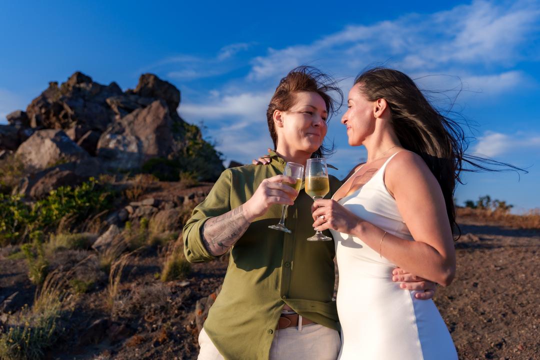 Two partners raising glasses at sunset on the caldera rim after their proposal