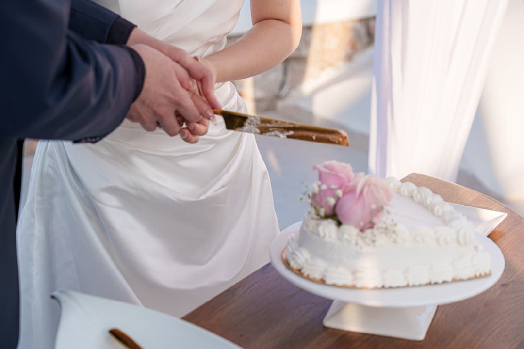 Four hands on one gold knife cutting a small heart-shaped wedding cake dressed with pink roses