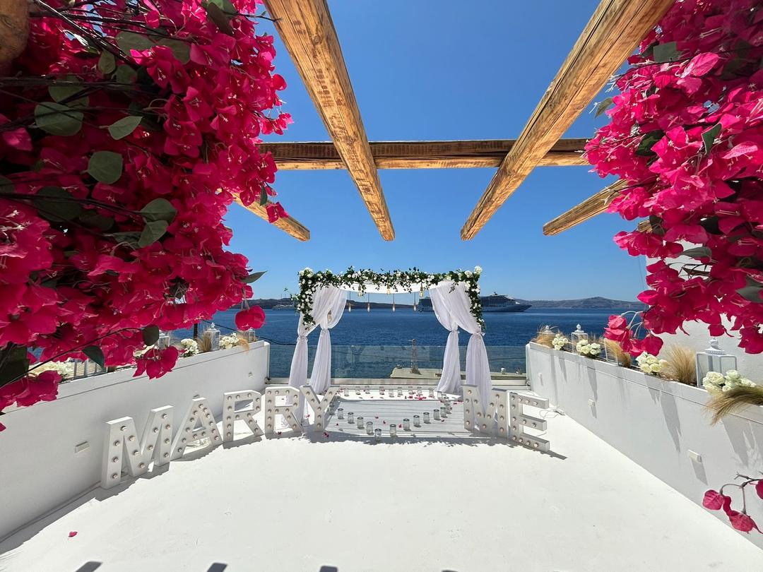 White proposal arch and Marry Me letters under magenta bougainvillea at a waterfront venue