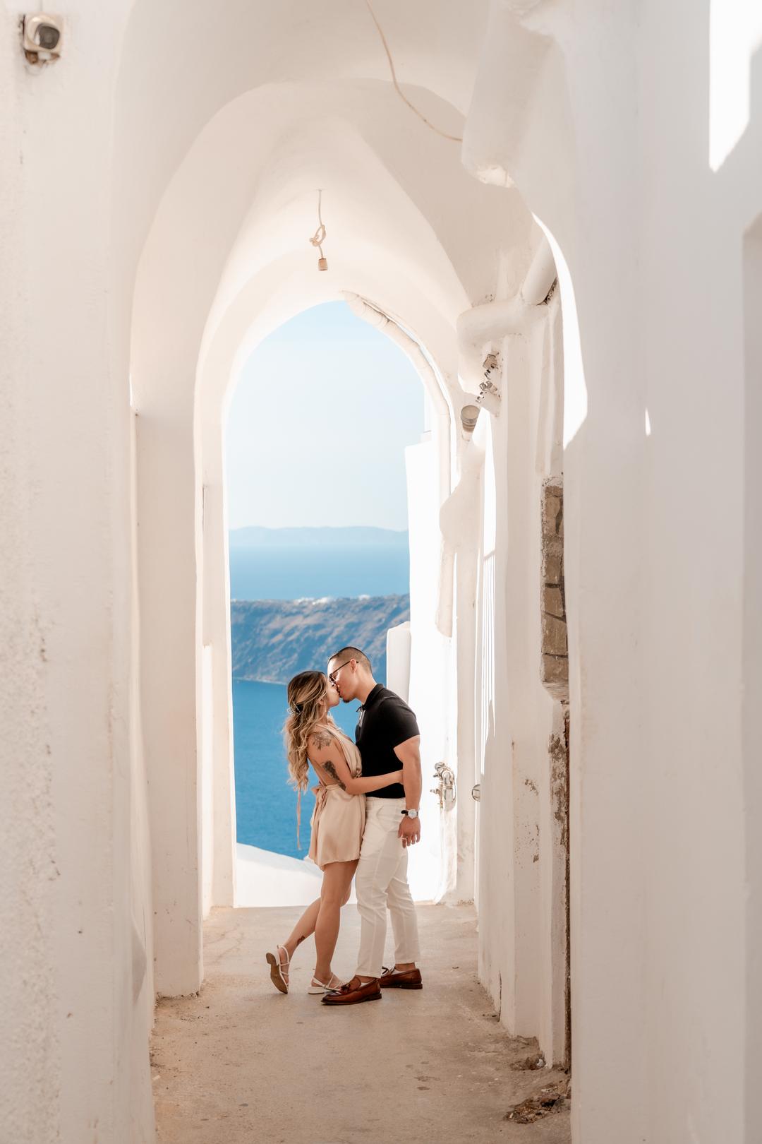 An embrace framed by a whitewashed arch with the caldera beyond