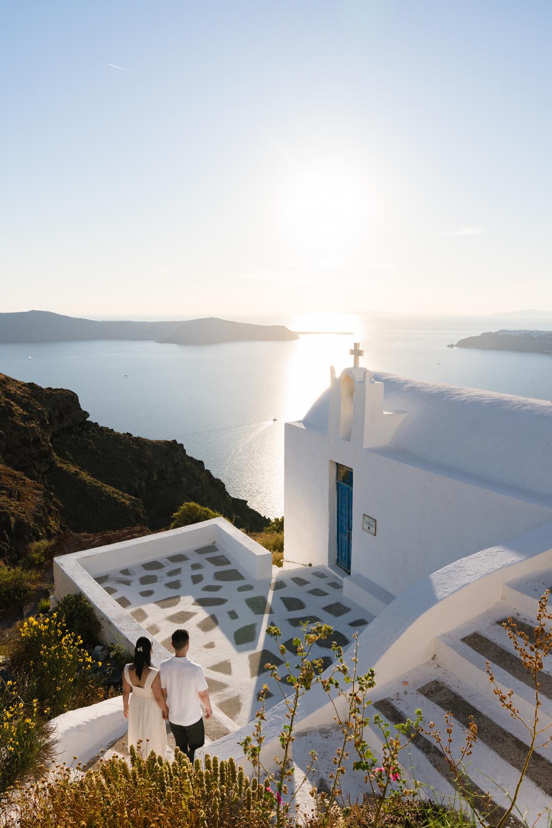 A whitewashed chapel and its cross above the caldera, the low sun laid across the water